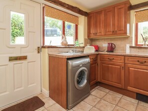 A compact kitchen with wooden cabinets, a built-in washing machine, and a window with a view of the outdoors. - The Retreat (Wellington)