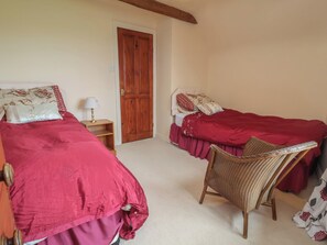 A bedroom with two beds, a wooden door, a nightstand, and a wicker chair. - The Retreat (Wellington)