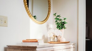 Un meuble blanc orné d’un motif géométrique, un miroir avec un cadre doré, un vase rempli de fleurs et une petite plante posée sur le dessus.