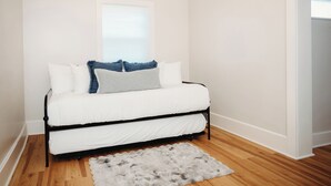Un canapé-lit blanc, un tapis moelleux, une fenêtre avec des stores et un plancher en bois.