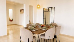 A dining area with a wooden table set for six, beige chairs, and a large mirror on the wall. - Villa Hanine S3 Piscine (Hammamet)