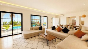 A modern living room with a pool view, large windows, and a dining area. - Villa Hanine S3 Piscine (Hammamet)