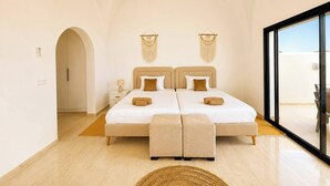 A bedroom with a large bed, a nightstand, a lamp, and a view through a glass door. - Villa Hanine S3 Piscine (Hammamet)