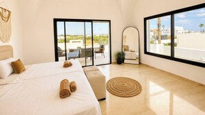 A bedroom with a bed, a large window, a mirror, and a view of the outdoors. - Villa Hanine S3 Piscine (Hammamet)