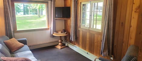 A cozy room with a wooden ceiling, a sofa, a chair, a television, and a window with curtains.
