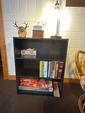 Une bibliothèque remplie de divers livres et jeux, une tête de cerf décorative et une lampe.