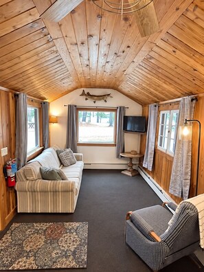 A cozy cabin interior with a sofa, armchair, and a flat-screen TV. - Pine Haven (Mercer)