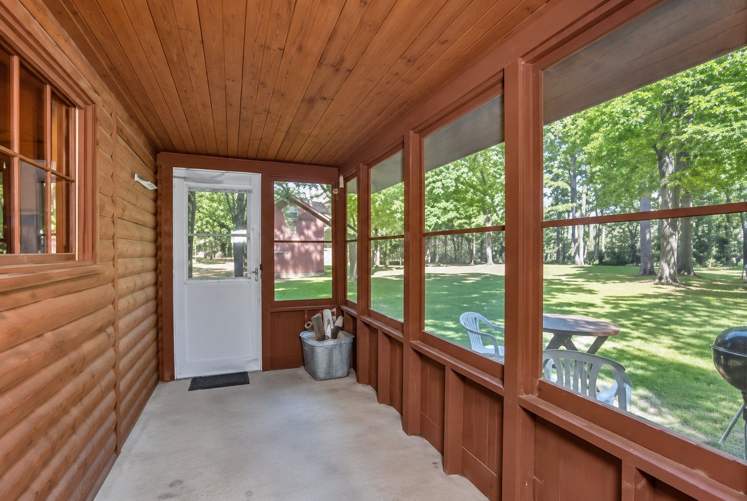 Screened porch with wooded views, outdoor seating, and a peaceful yard
