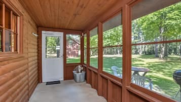 Screened porch with wooded views, outdoor seating, and a peaceful yard