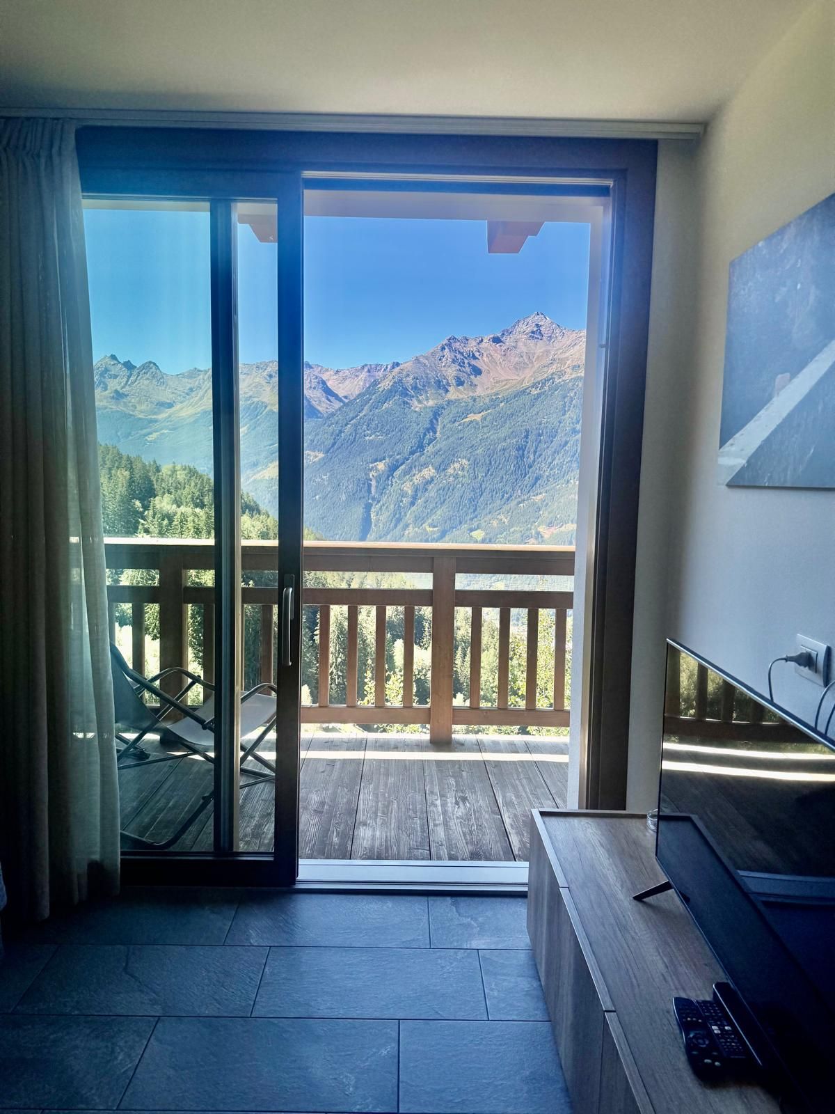 Une pièce dotée d’une grande porte-fenêtre coulissante donnant sur un balcon avec vue sur les montagnes.