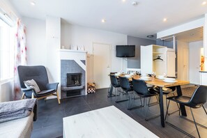 A modern living room with a fireplace, dining area, and a TV mounted on the wall. - Levin Kotka E1 & E2 -  United Apartments (Kittilä)