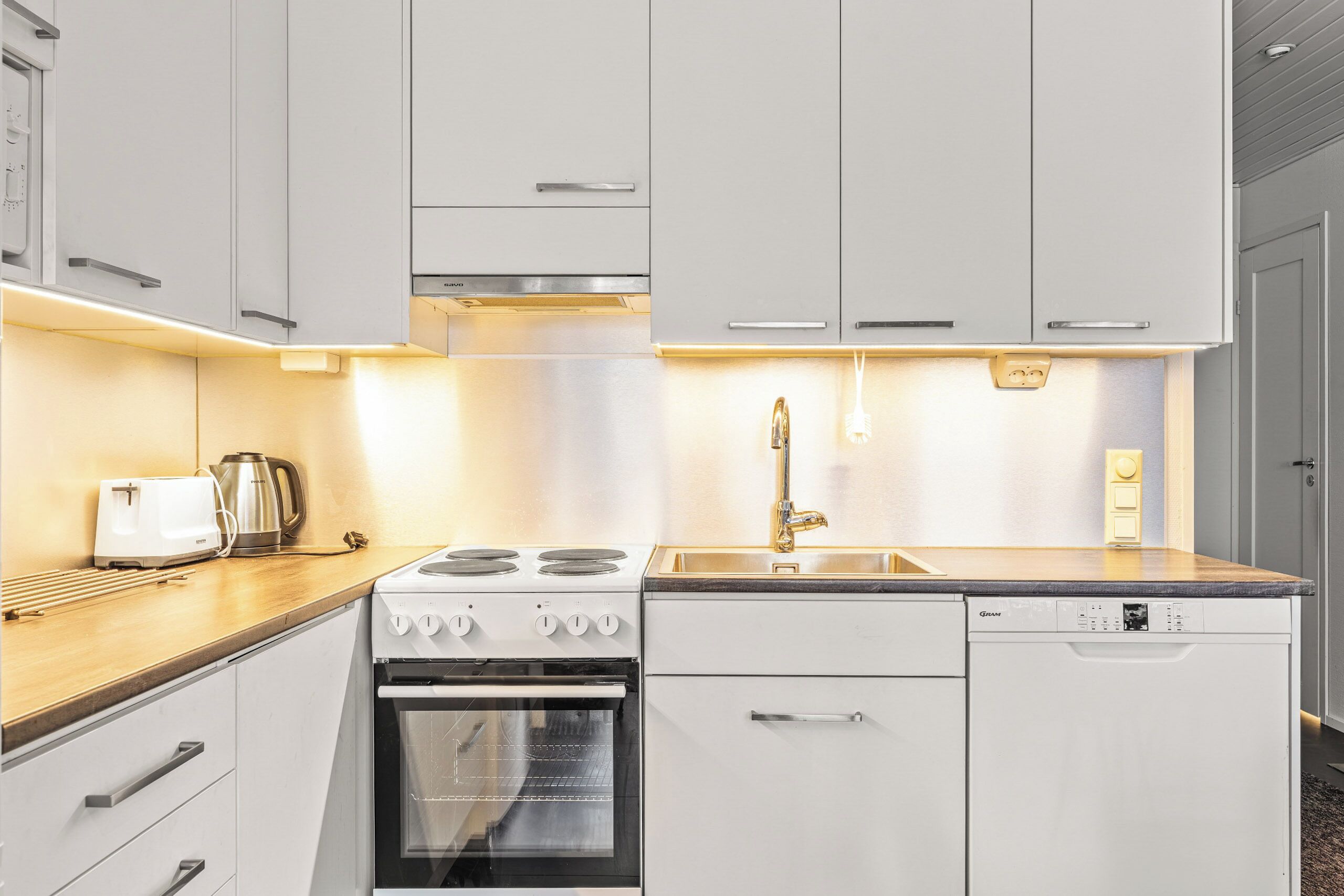 A modern kitchen with white cabinets, a stove, an oven, a dishwasher, and a wooden countertop.