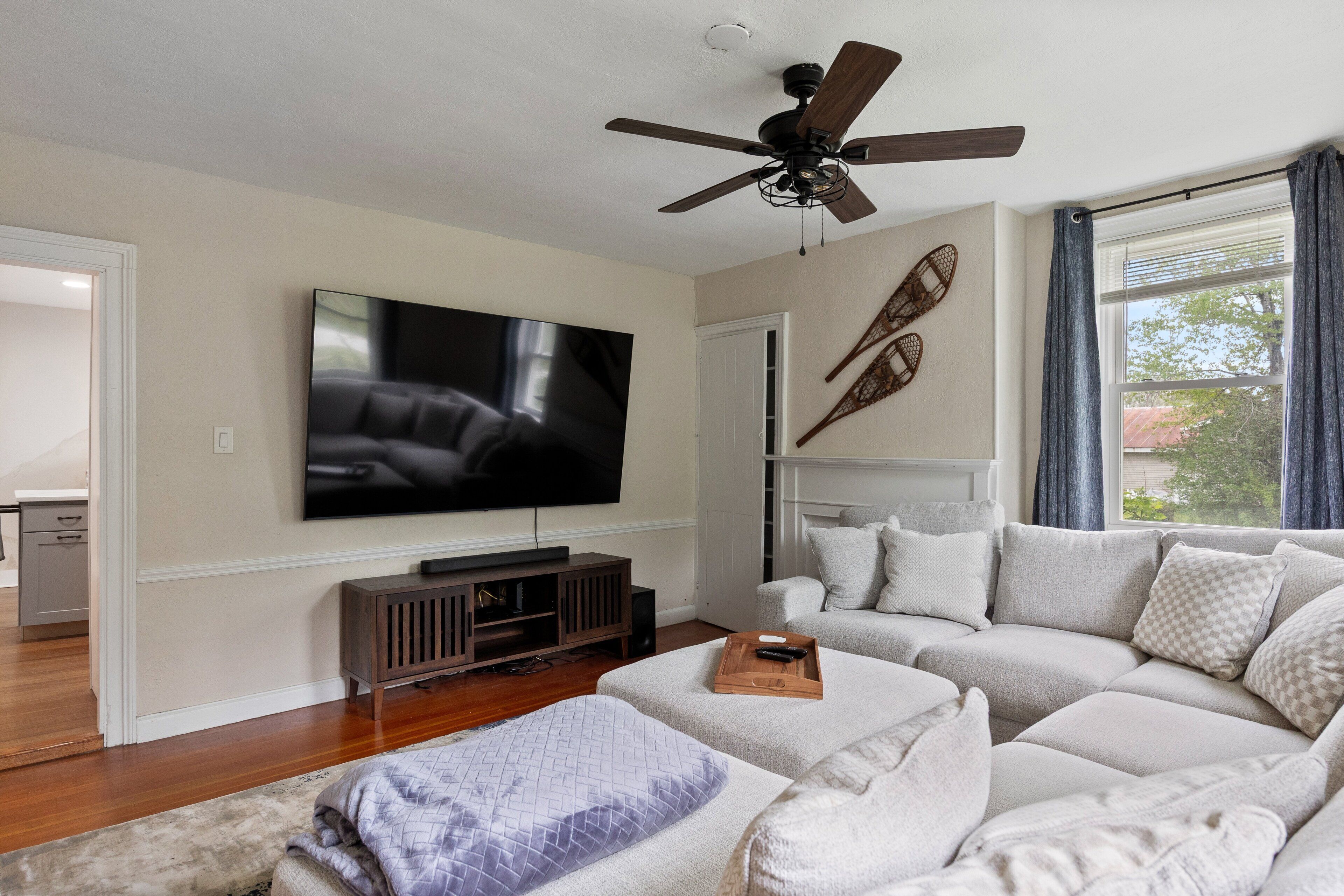 Een woonkamer met een grote flatscreen-tv, een plafondventilator, een hoekbank en een houten salontafel.
