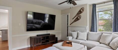 Een woonkamer met een grote flatscreen-tv, een plafondventilator, een hoekbank en een houten salontafel.