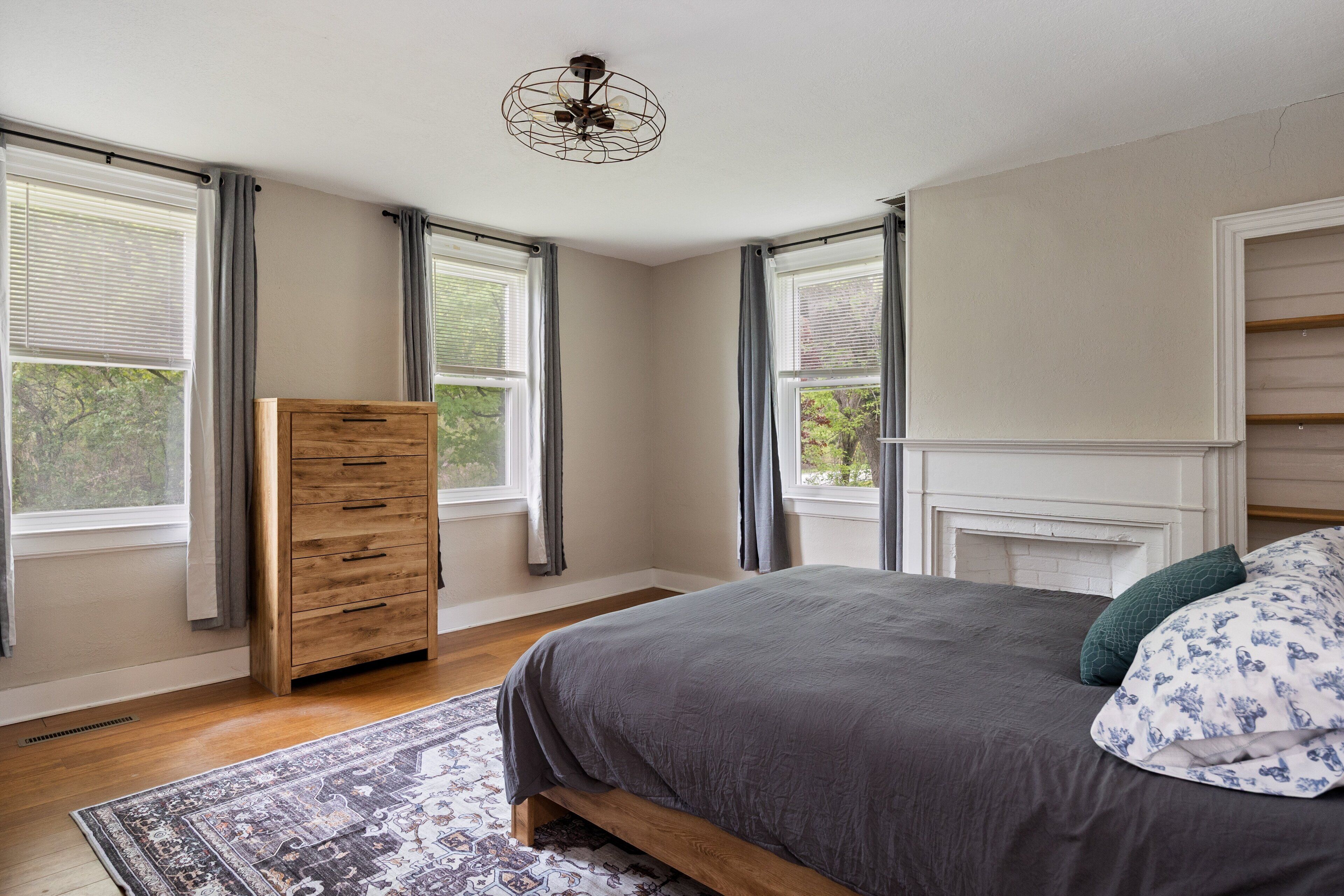 Quarto com cama, penteadeira, lareira e janelas amplas.