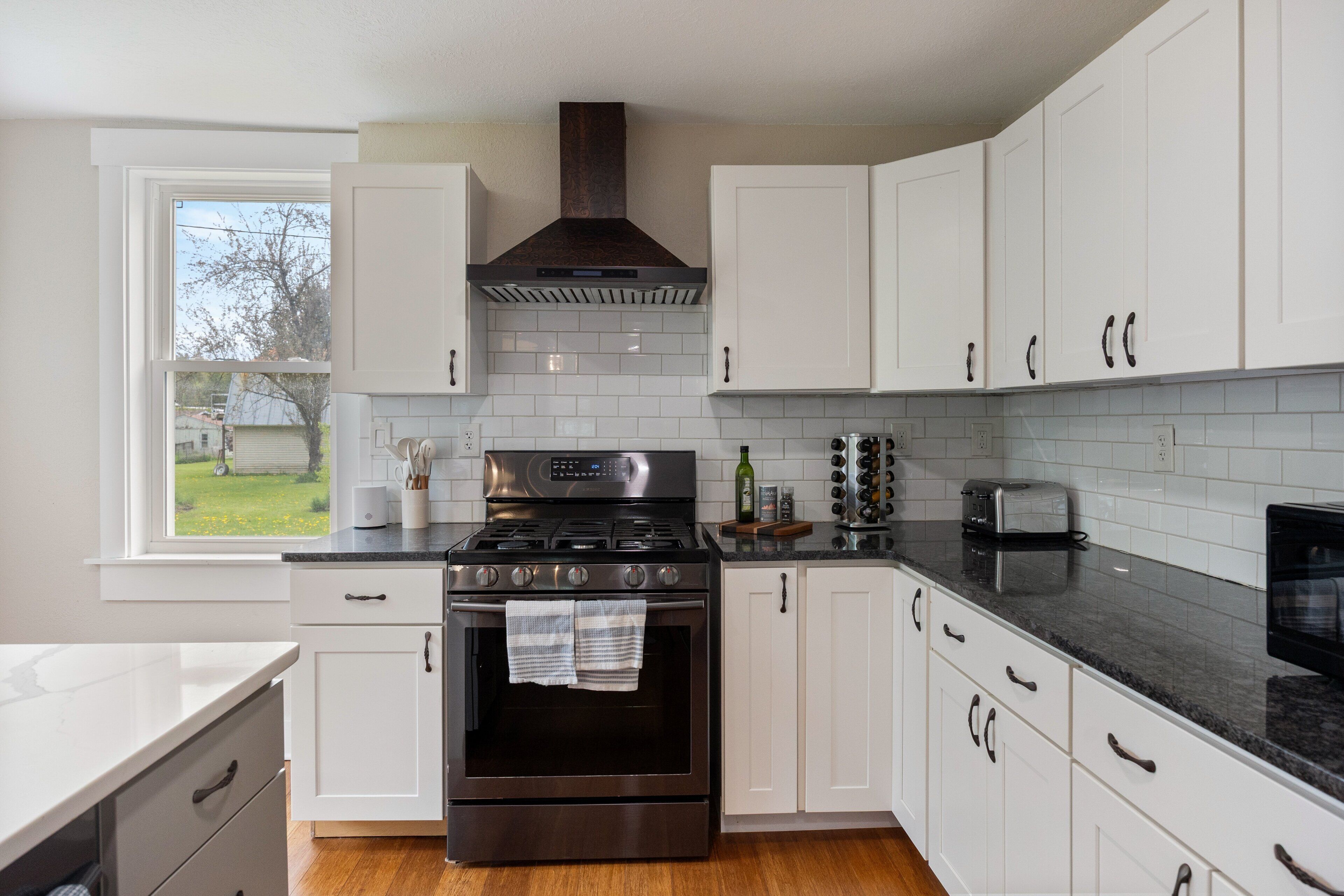 A modern kitchen with white cabinets, a stainless steel stove, and a window overlooking a yard.