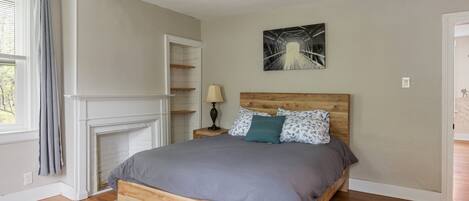 Un dormitorio con una cama de madera, una chimenea, una mesita de noche y un cuadro en la pared.