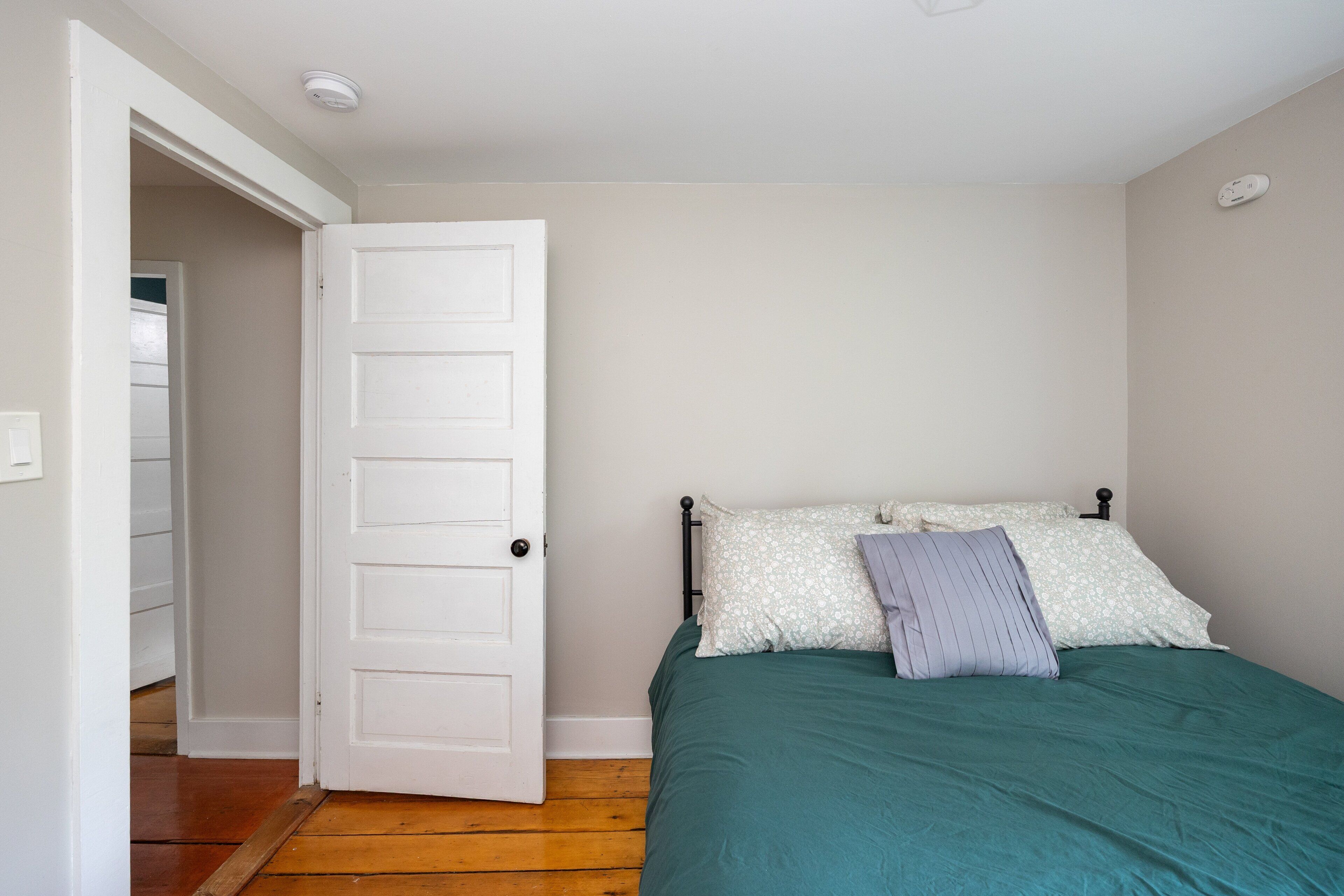 A bedroom with a bed, a door, and a wooden floor.