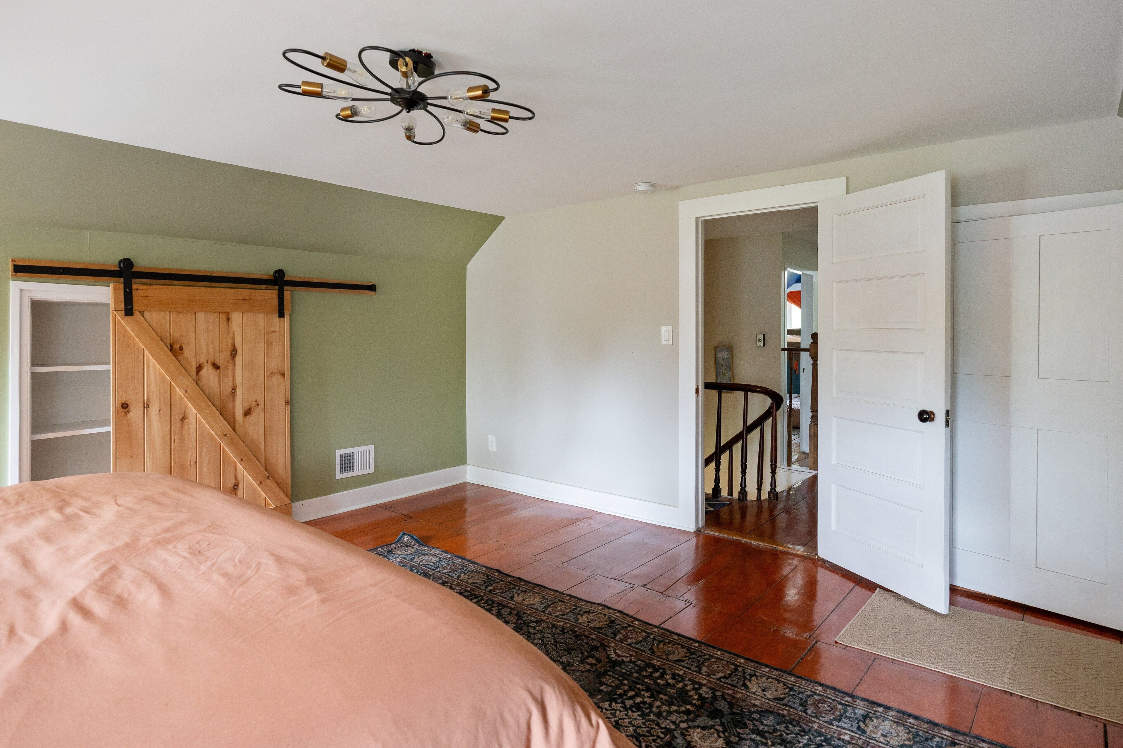 A bedroom with a bed, a wooden closet, a ceiling fan, and a door leading to another room.