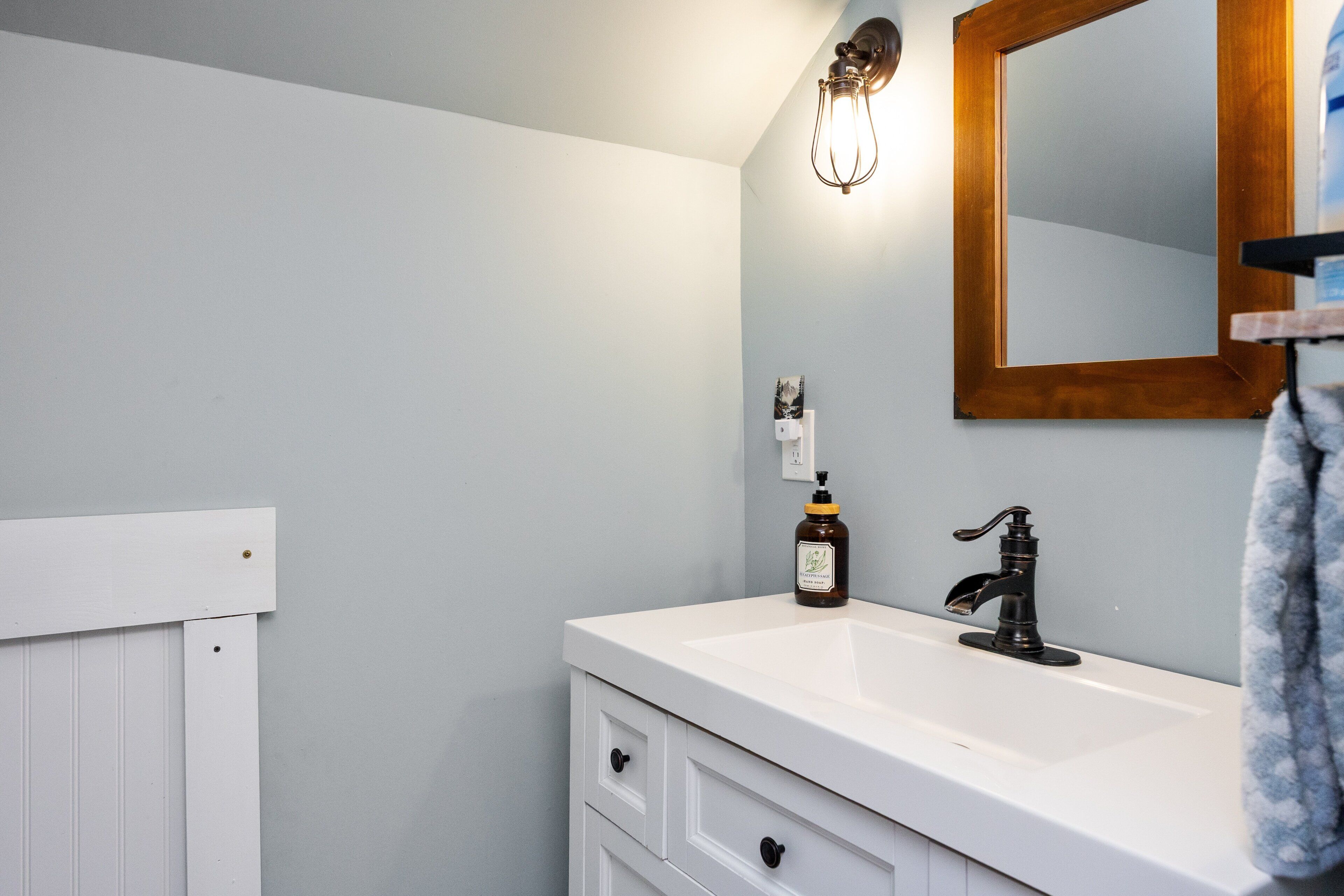 Une salle de bain avec un meuble-lavabo blanc, un robinet noir, un miroir encadré en bois et un luminaire fixé au mur.