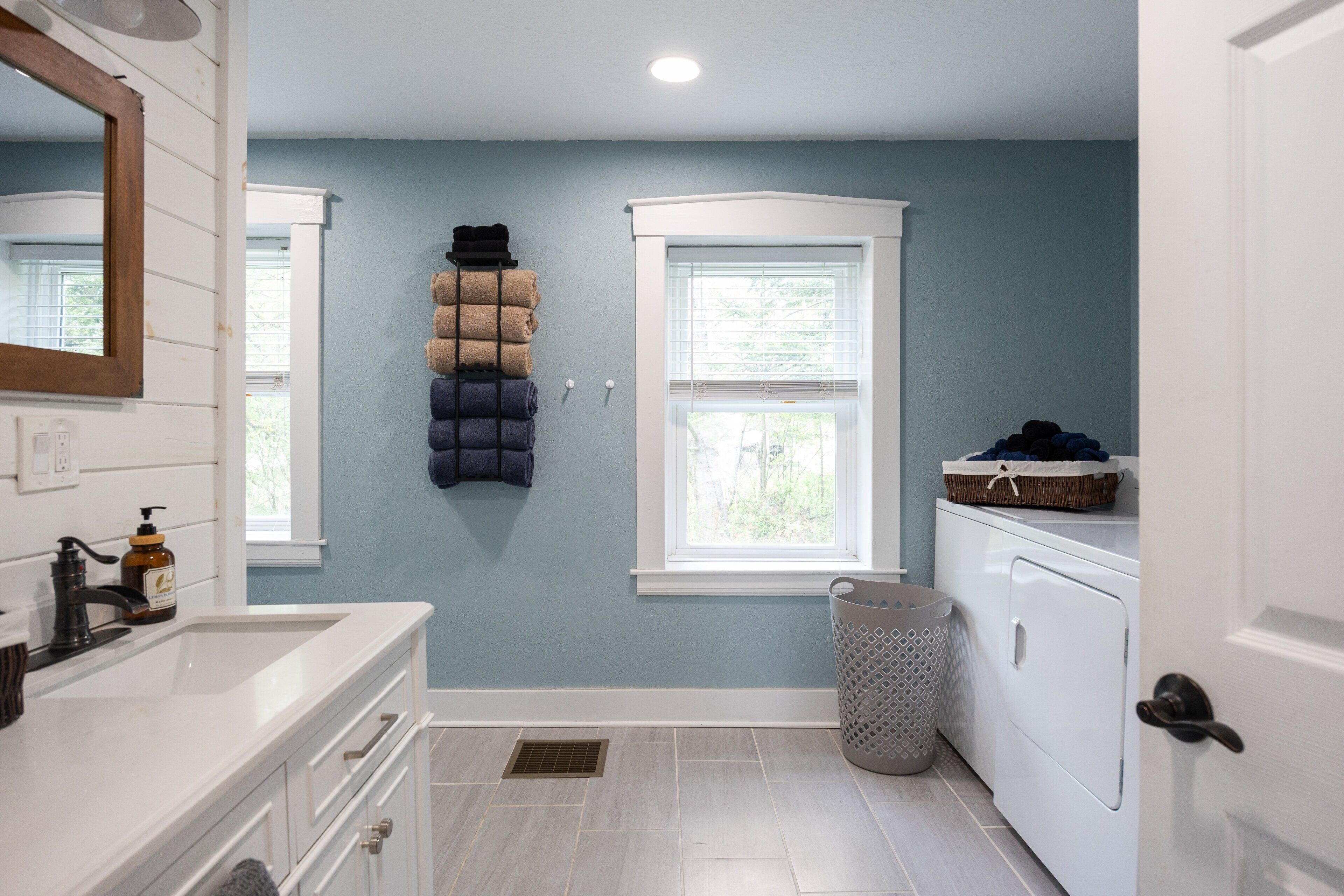 A bathroom with a white vanity, a mirror, a window, a laundry basket, and a washing machine.