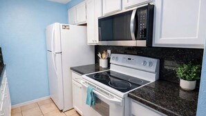 Una cucina compatta con mobili bianchi, un forno a microonde nero, un piano cottura bianco e un frigorifero.