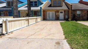 Una strada residenziale con case, un vialetto in cemento e un recinto bianco.