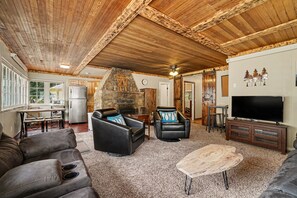 Ein großzügiger Wohnbereich mit Kamin aus Stein, Ledersofas, einem Flachbildfernseher und einer Holzbalkendecke.