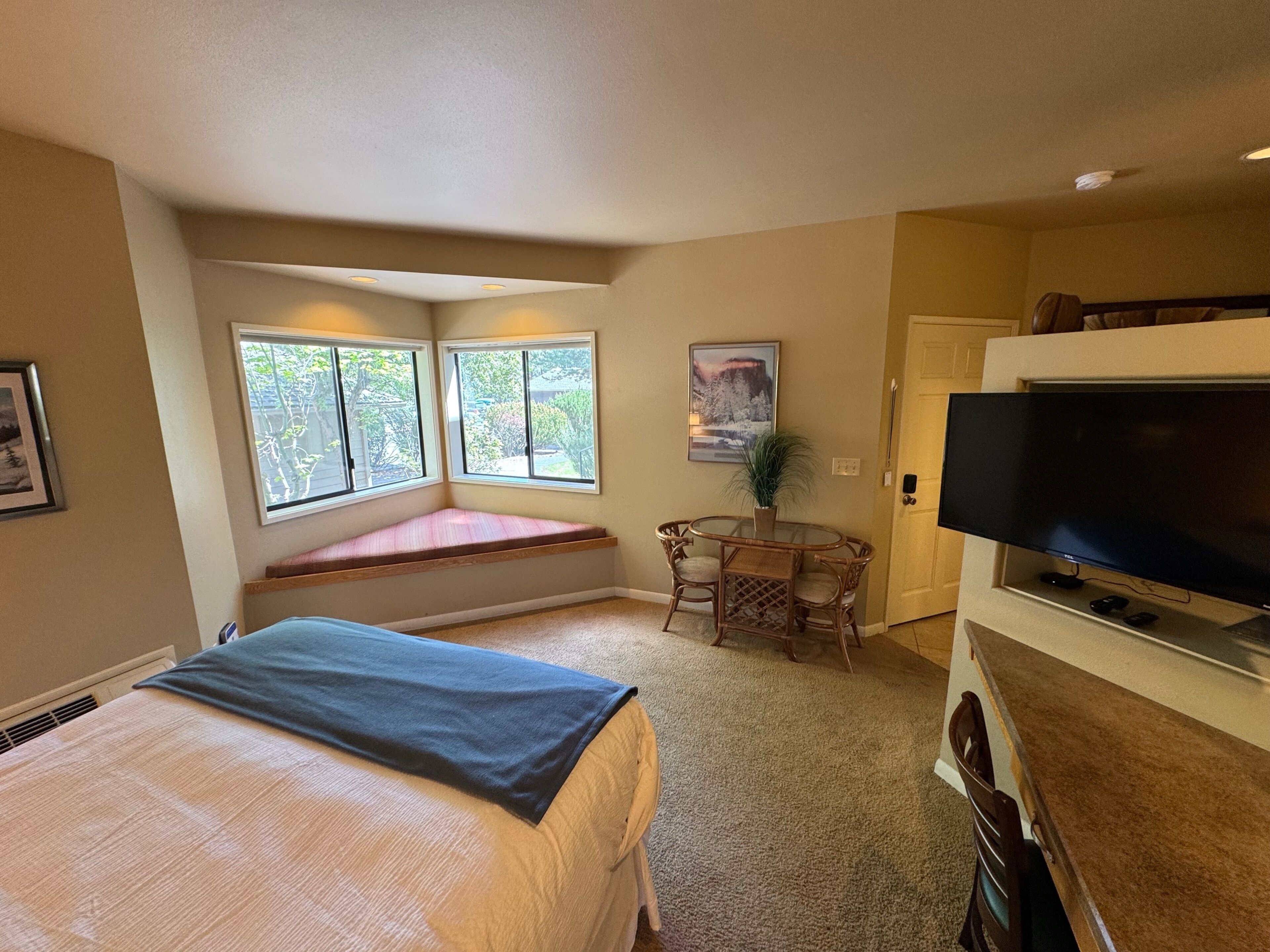 Ein Schlafzimmer mit Bett, Fensterbank, Fernseher und einem kleinen Tisch mit Stühlen.