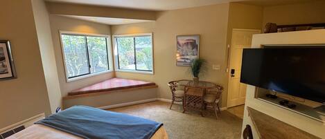 Ein Schlafzimmer mit Bett, Fensterbank, Fernseher und einem kleinen Tisch mit Stühlen.