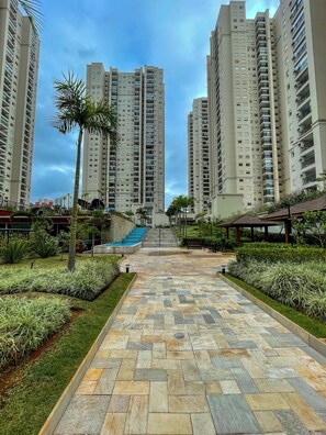 A pathway leading to a building entrance with a staircase, surrounded by greenery and tall residential buildings. - Smart Studio 01206 - Near Maia Shopping Mall, Leisure Area, Parking Space (Guarulhos)