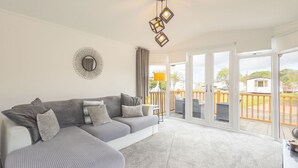 Un salon moderne avec un canapé d’angle, un luminaire au plafond et une vue sur une terrasse extérieure, accessible par de grandes portes-fenêtres coulissantes.