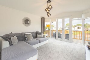 A modern living room with a sectional sofa, a ceiling light fixture, and a view through large sliding glass doors to an outdoor deck. - Host & Stay | Hazel Retreat (Felton)