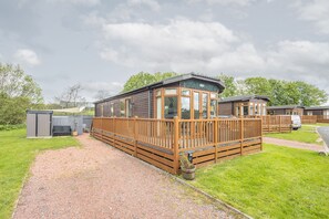 A row of wooden mobile homes with a gravel path leading to the entrance, surrounded by green grass and trees. - Host & Stay | Hazel Retreat (Felton)