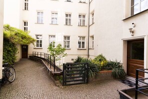 A courtyard with a cobblestone path, a bicycle, a gate, and a building with multiple windows and a door. - Garbary Studio - Old Town, Top Location - by Rentujemy (Poznań)