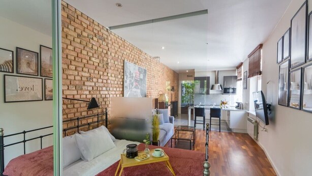 Um apartamento moderno com parede de tijolos, uma cama, um sofá, um espaço de refeições e uma cozinha.