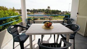 Een balkon met een tafel, stoelen, een fruitschaal en uitzicht op een park en gebouwen.