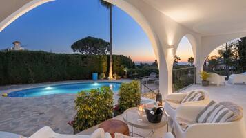 A poolside area with a view of the sunset, outdoor seating, and a well-maintained garden.