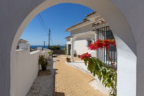 A narrow pathway leading to a building with a white facade, a tiled roof, and a view of the sea. - Elegant Villa With Pool Terrace in Marbella (Marbella)