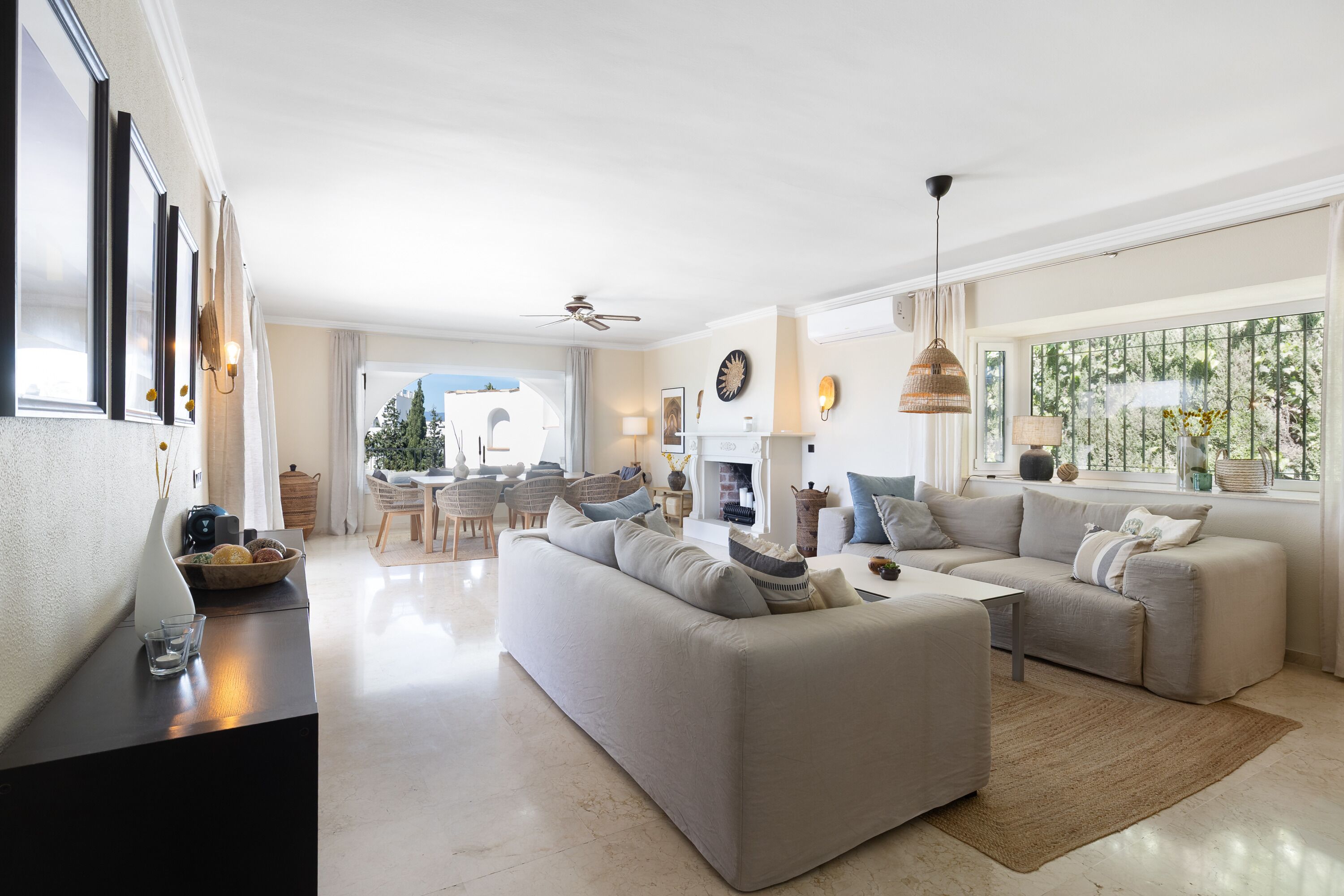 A spacious living room with a large sofa, a coffee table, and a fireplace. There is a dining area with chairs and a table visible in the background.