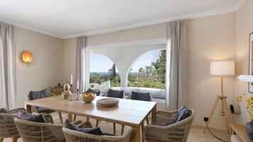 A dining area with a wooden table, wicker chairs, and a view through large windows.