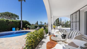 A poolside area with outdoor seating, a view of the sea, and a well-maintained garden.