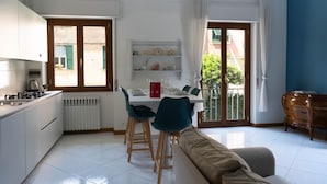 Ett modernt kök med vita skåp, ett matbord med plats för fyra personer och en soffa i vardagsrummet.
