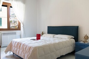 A neatly made bed with a blue headboard, a bedside table with a lamp, and a window with curtains. - Green Terrace Santa Margherita by Wonderful Italy (Santa Margherita Ligure)