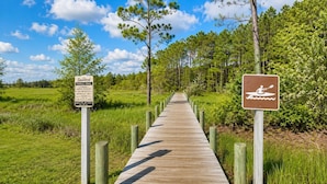 A wooden boardwalk leading through a natural area with signs indicating a paddle trail and park facilities. - Salty Paws Cottage - Where Coastal Comfort Meets Pet-Friendly Living! (Beaufort)