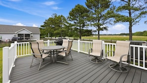 A deck with outdoor furniture, a grill, and a view of a house and trees. - Salty Paws Cottage - Where Coastal Comfort Meets Pet-Friendly Living! (Beaufort)