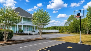 A basketball court with a hoop, a building with a porch, and trees. - Salty Paws Cottage - Where Coastal Comfort Meets Pet-Friendly Living! (Beaufort)