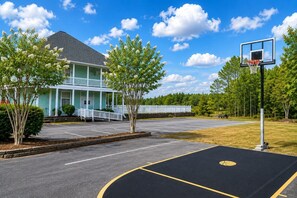 En basketplan med en basketkorg, en byggnad med en veranda och träd.