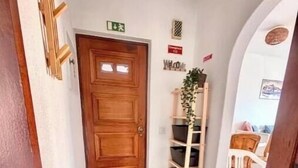 Un couloir avec une porte en bois, une pancarte de bienvenue, une plante et un porte-chaussures.