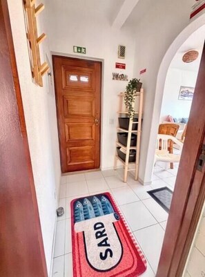 A hallway with a wooden door, a welcome sign, a plant, and a shoe rack. - Beach Front + Castle and sea view Home in Heart of Ferragudo (Ferragudo)